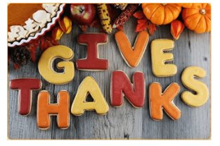 Text in iced cookies; "Give Thanks". with corn, pumpkins, with gray wood background.