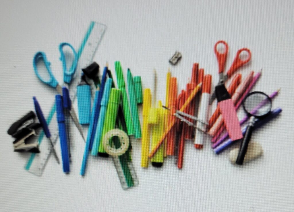 A picture of colorful school utensils, scissors, staple removers, ruler, magnifying glass, protractor, markers,  highlighters, pencils, etc.  